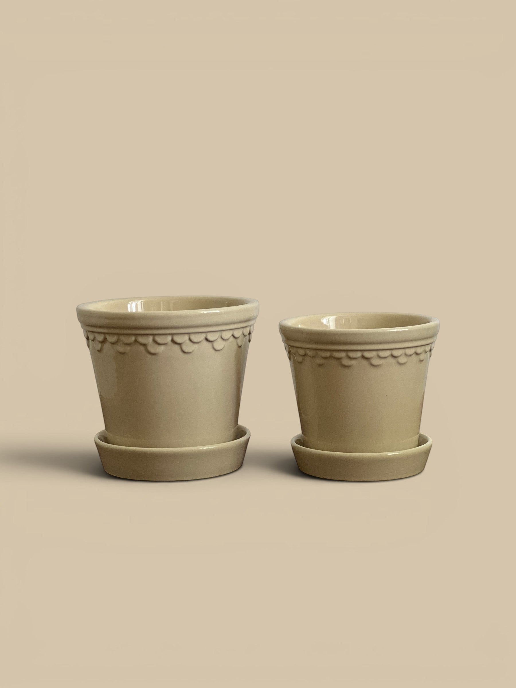 Homestyle Collective two glazed sandstone pots with scalloped trim and matching saucers, available in small and medium sizes.
