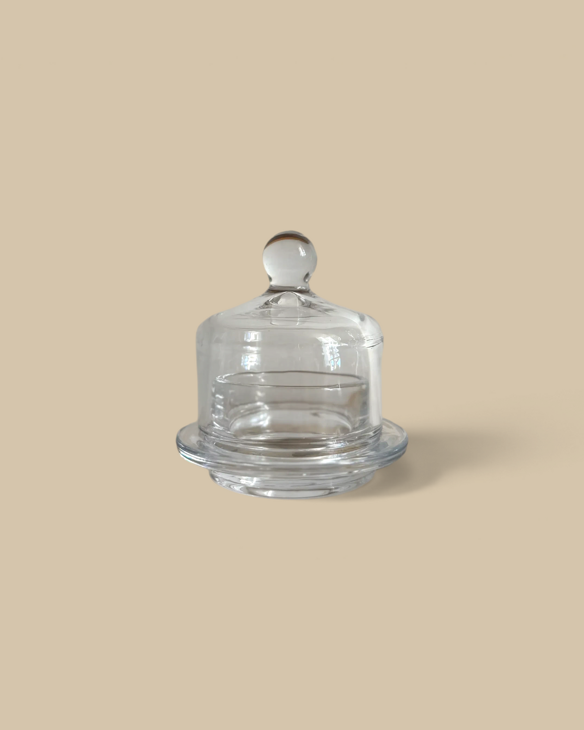 Homestyle Collective small clear glass butter dish with a domed lid and round handle on a stone surface