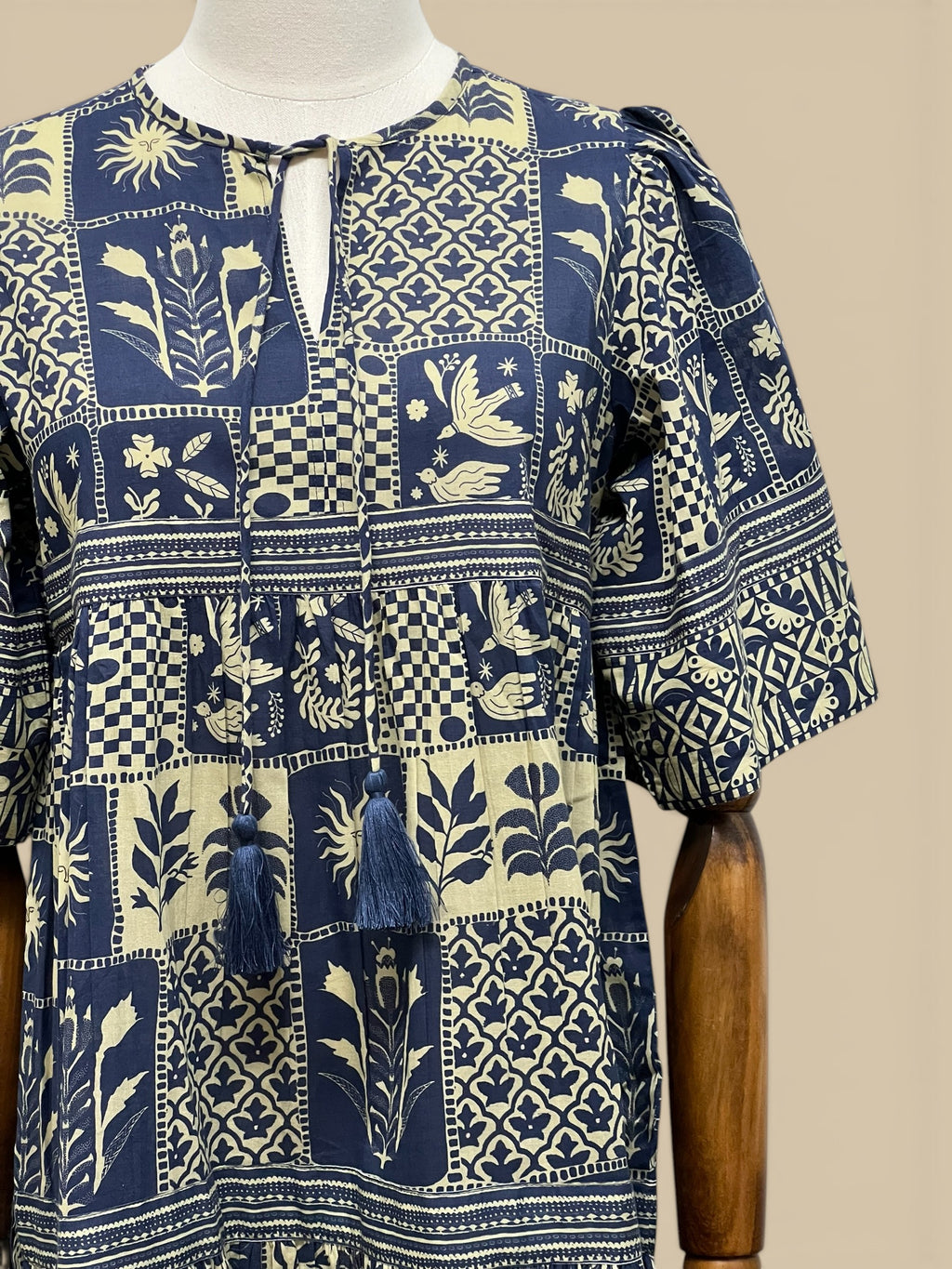 Homestyle Collective Sohana Patches Dress, a blue and cream 100% cotton midi dress with block print patterns, puff sleeves, and tassel tie neckline.