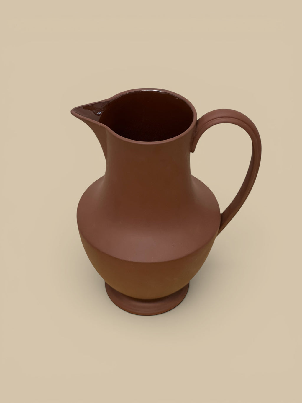 Homestyle Collective terra cotta stoneware pitcher with a matte finish and a glossy interior. Features a wide base, curved body, and elegant spout.