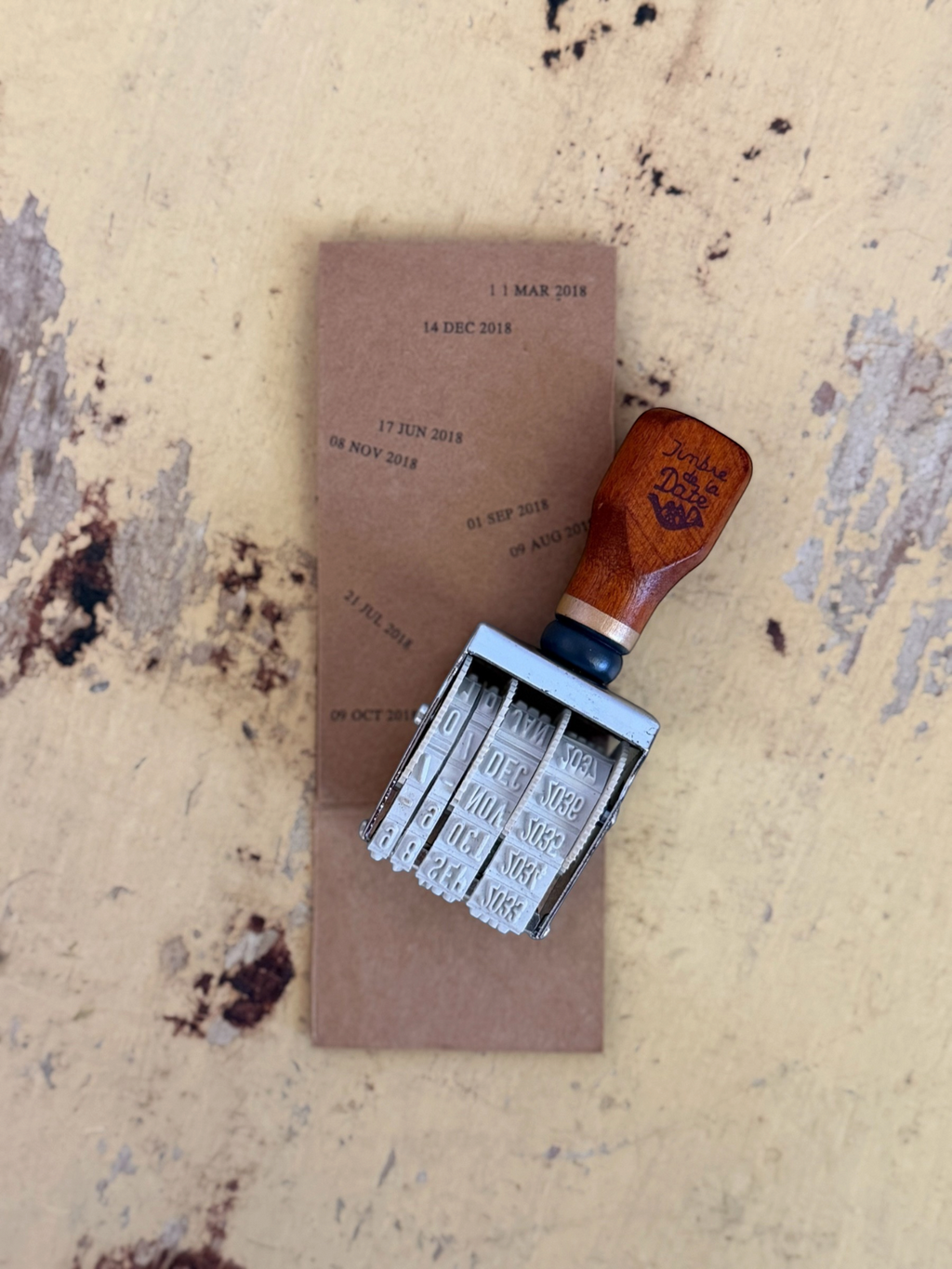 Homestyle Collective vintage-style wooden handle date stamp with adjustable rotating wheels on a rustic textured surface
