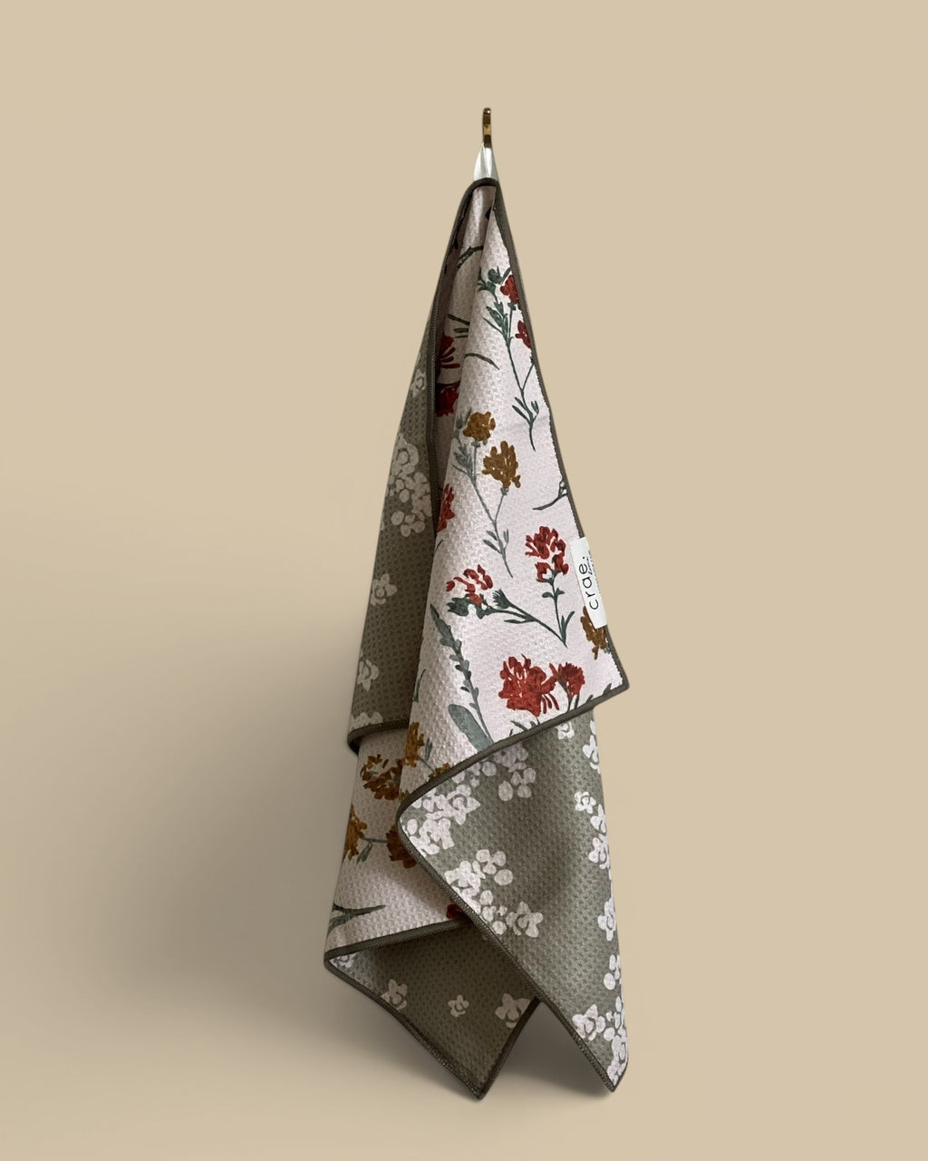 Homestyle Collective waffle weave hand towel with a floral print in red, white, and gold on a light background and green.
