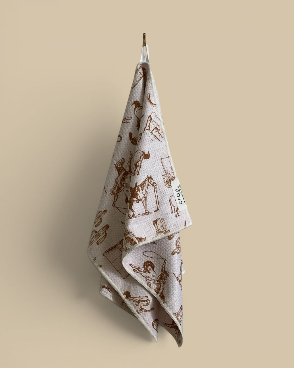 Homestyle Collective light pink waffle weave hand towel with brown cowboy and western-themed print.