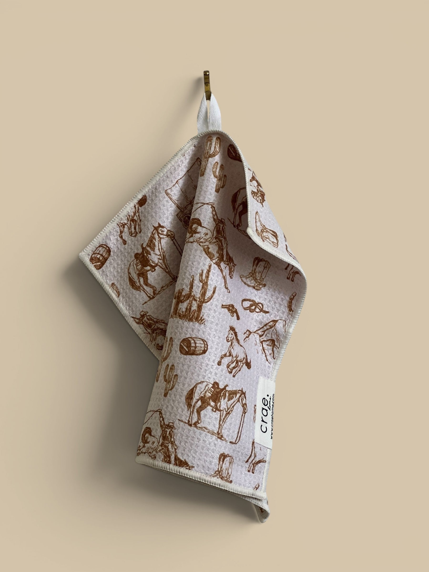 Homestyle Collective Waffle Weave Washcloth with cowboy, horse, cactus, and boot print. White with brown graphic.