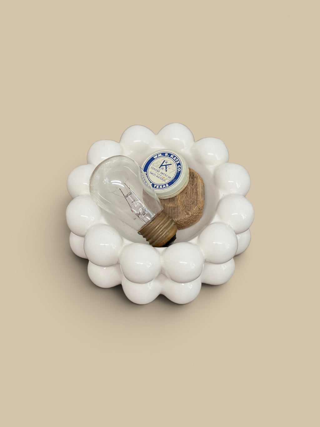 Homestyle Collective white stoneware bowl with raised bubble details, holding a vintage lightbulb and small wooden piece.
