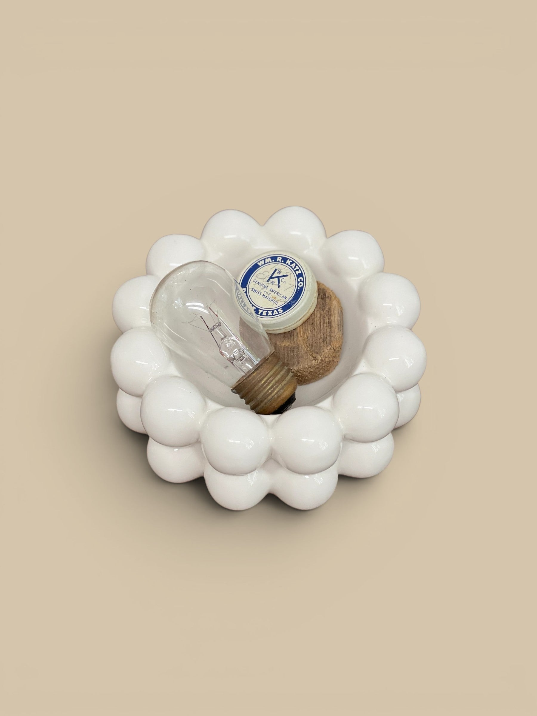 Homestyle Collective white stoneware bowl with raised bubble details, holding a vintage lightbulb and small wooden piece.