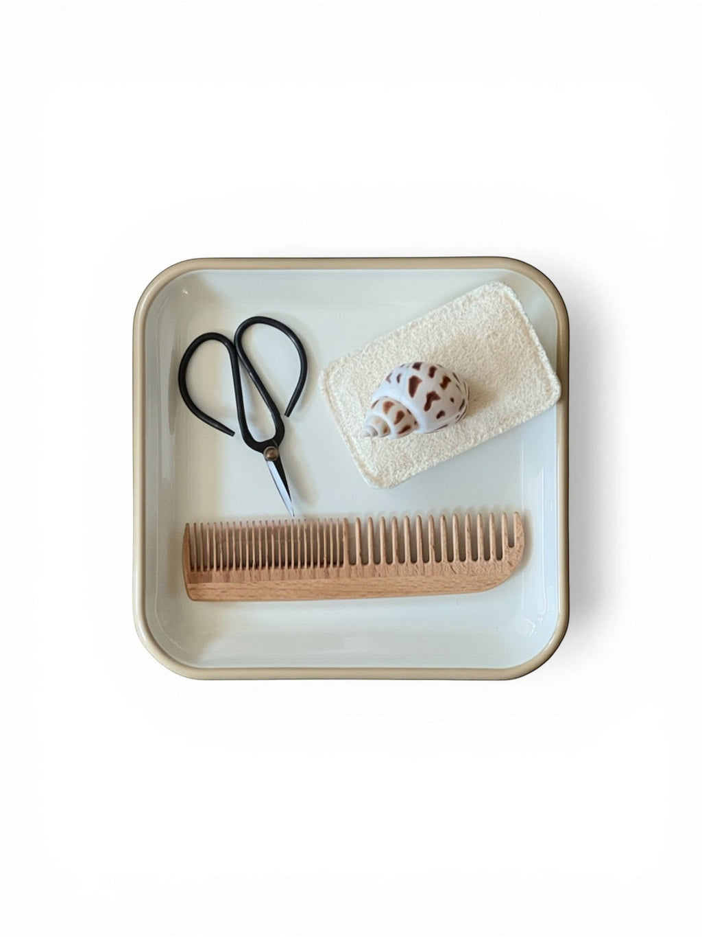 Homestyle Collective white enameled square plate with comb, scissors, and shell.