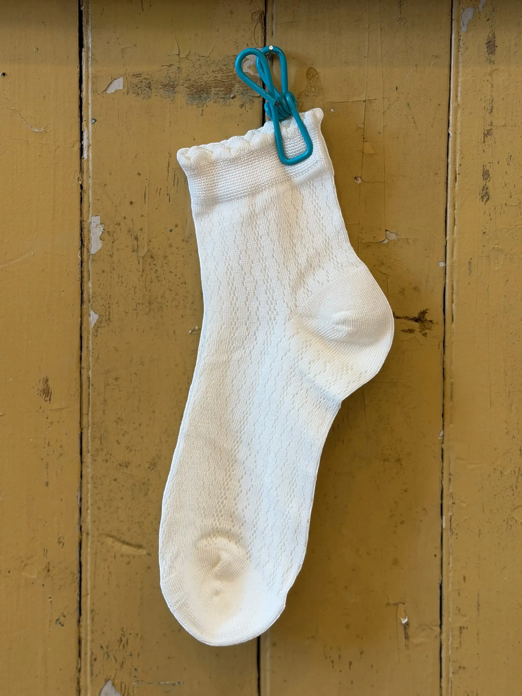 Homestyle Collective white ankle socks with mesh texture and a delicate ruffle cuff hanging on a wooden wall.