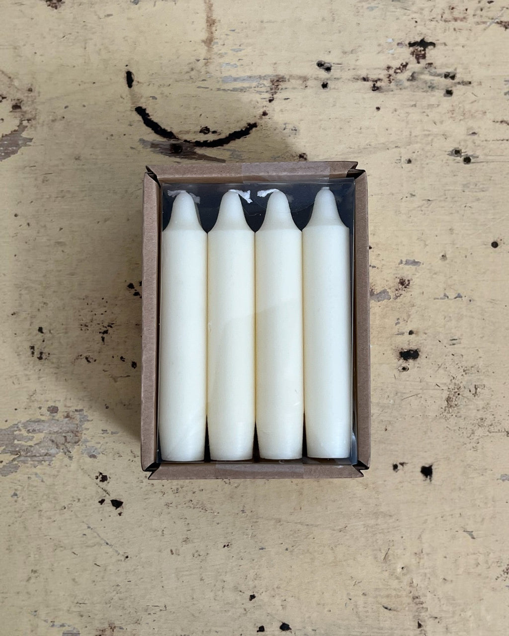 Homestyle Collective set of four unscented white 5-inch taper candles in a brown cardboard box on a rustic surface.