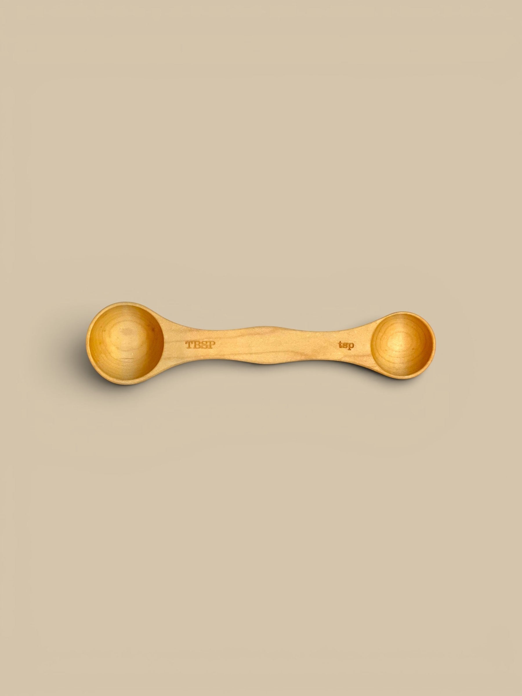 Homestyle Collective set of 3 double-sided wooden measuring spoons in light, medium, and dark wood finishes. Each spoon is labeled TBSP and tsp.