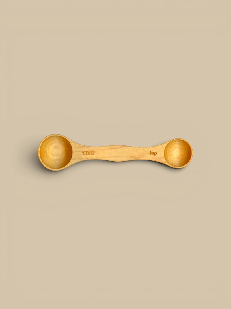 Homestyle Collective set of 3 double-sided wooden measuring spoons in light, medium, and dark wood finishes. Each spoon is labeled TBSP and tsp.