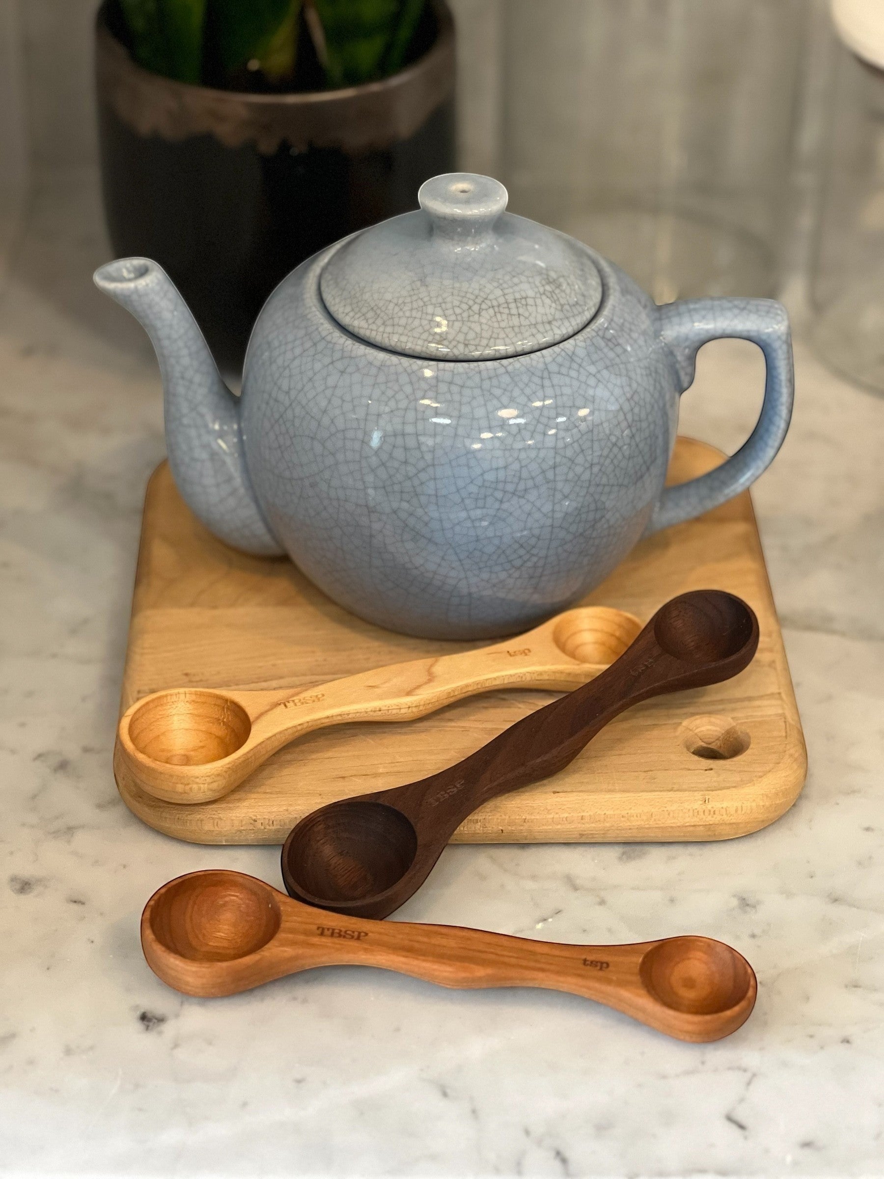 Homestyle Collective wooden measuring spoons in light, medium, and dark wood finishes, featuring tablespoon and teaspoon ends.